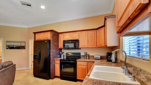 A kitchen with wooden cabinets, a black refrigerator, a stove, a microwave, a sink, and a window with a view of buildings.
