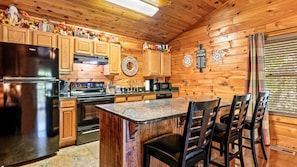 Une cuisine rustique aménagée dans une cabane en bois, avec un îlot central, des meubles de rangement en bois, un réfrigérateur, une cuisinière et une machine à café.