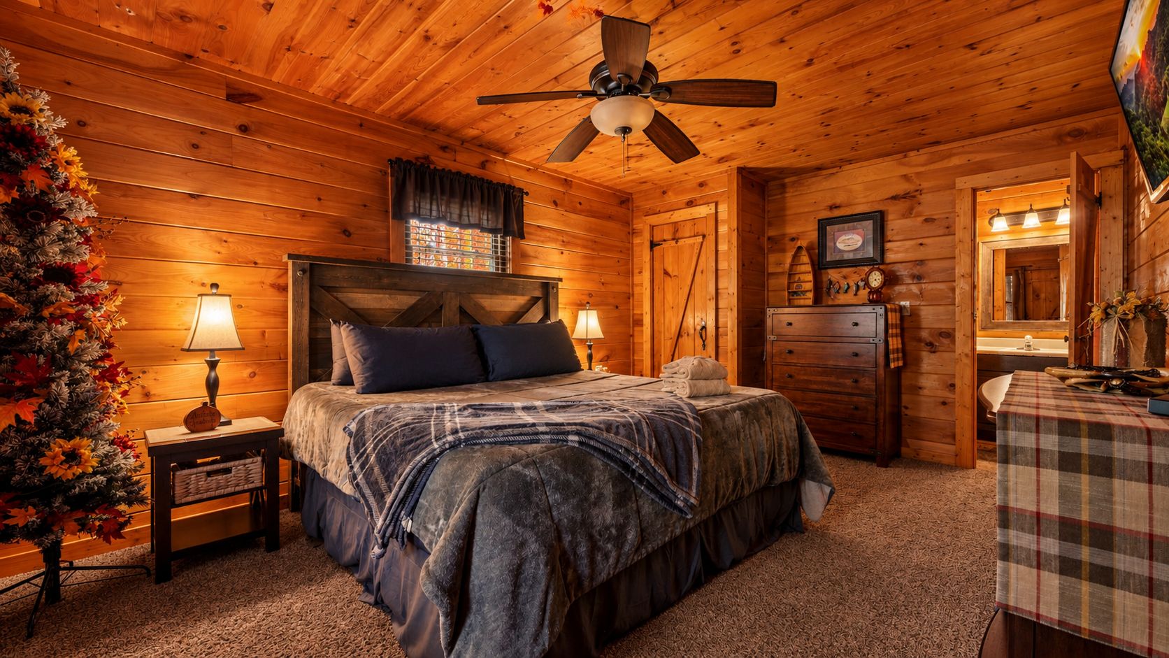 Ein gemütliches Schlafzimmer in einer Blockhütte mit einem Bett, zwei Nachttischen mit Lampen, einer Kommode und einer karierten Tischdecke.