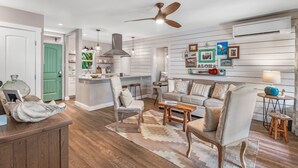 A modern kitchen with a central island, a dining area with a sofa and chairs, and a living room with a large sofa and a coffee table. - New! The Aloha Cottage in Puamana, Maui Hawaii (Lahaina)