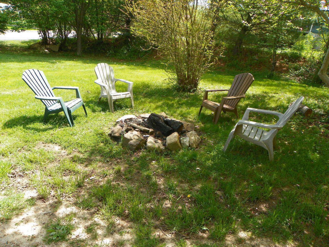 A grassy outdoor area with a fire pit and four Adirondack chairs.