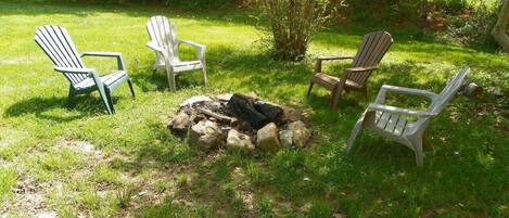 A grassy outdoor area with a fire pit and four Adirondack chairs.