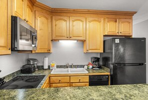 Une cuisine avec des meubles de rangement en bois, un réfrigérateur noir, un four à micro-ondes, une cuisinière, un évier et un lave-vaisselle.