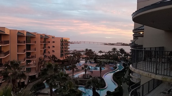 A resort with multiple swimming pools, palm trees, and a view of the sea and a bridge.