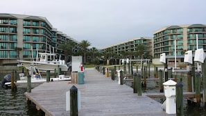 A marina with boats docked, wooden walkways, and modern buildings with balconies in the background.