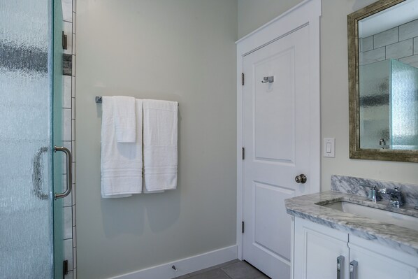 A bathroom with a white door, a towel rack with two towels, a marble sink, and a mirror with a gold frame.