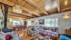 A cozy living room with a large sectional sofa, a smaller couch, and a wooden floor. There is a dining area with a table and chairs in the background.
