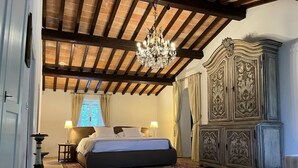 A bedroom with a large bed, a chandelier, a wooden ceiling, and a vintage-style wardrobe. - Totally Private18th Century Stone Villa with 15mt heated Pool (Monte Castello di Vibio)