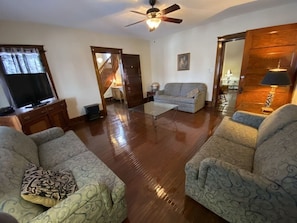 A living room with a wooden floor, two patterned sofas, a glass coffee table, and a ceiling fan.