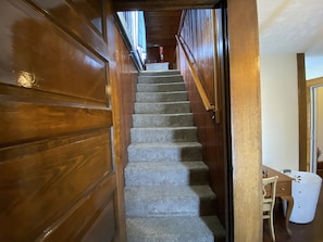Stairs lead to an upper floor with a table and chair below.