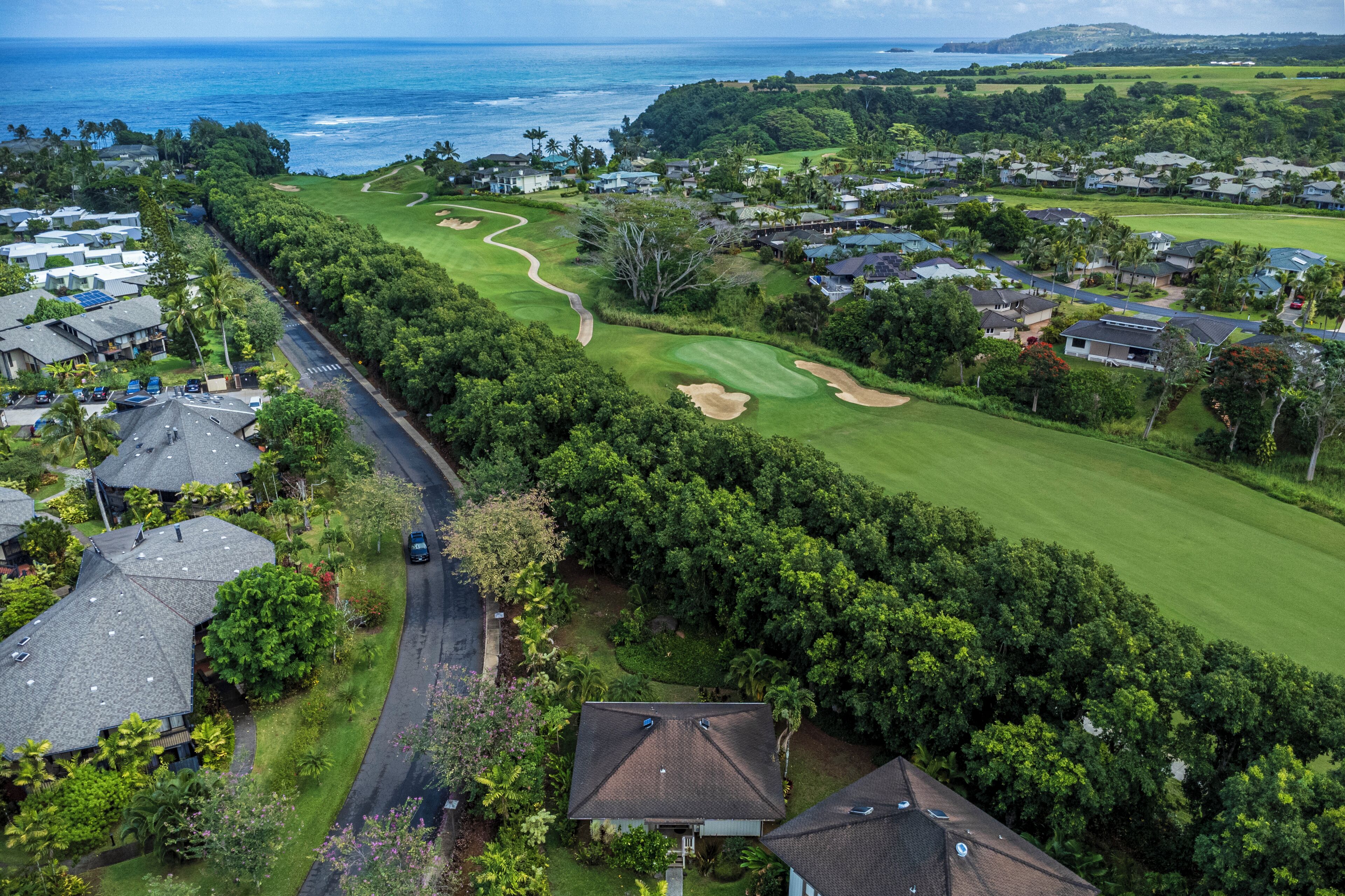 Vista aérea de un campo de golf con una carretera que lo bordea, rodeado de casas residenciales y exuberante vegetación.