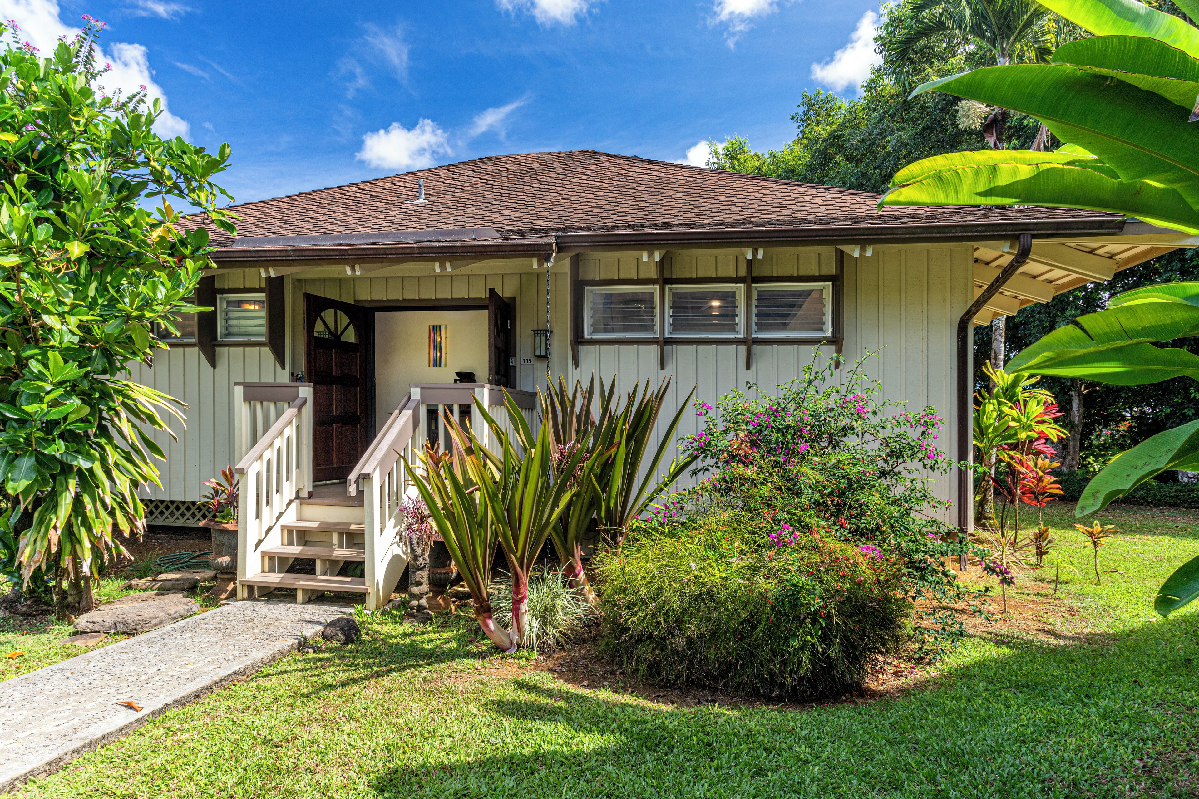 A single-story house with a front porch, a small garden, and a clear blue sky.