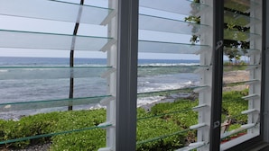 Vista a través de una ventana con múltiples cristales, hacia una playa con olas y vegetación.