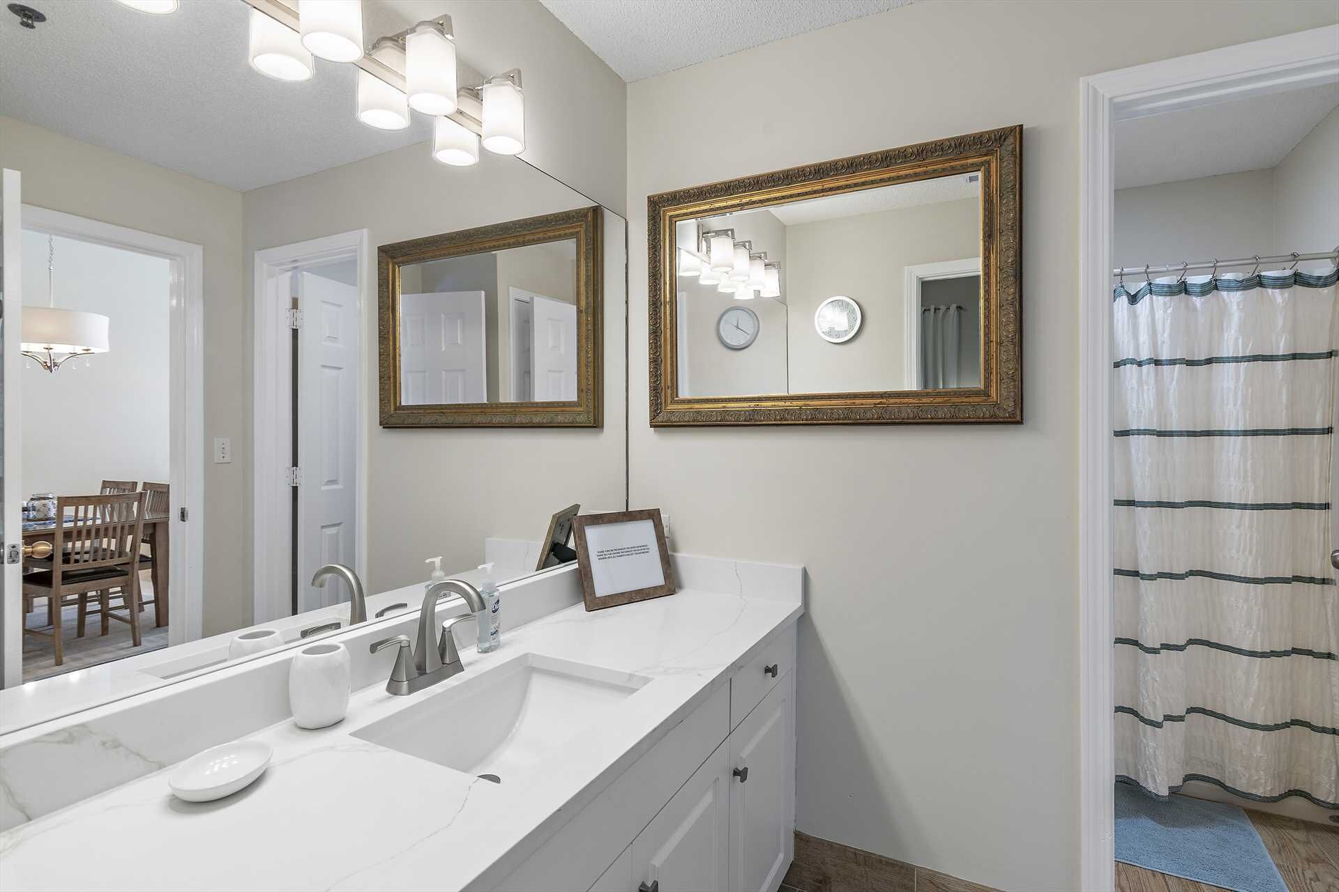 A bathroom with a white vanity, two mirrors with gold frames, a shower curtain, and a clock on the wall.