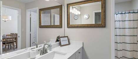 A bathroom with a white vanity, two mirrors with gold frames, a shower curtain, and a clock on the wall.