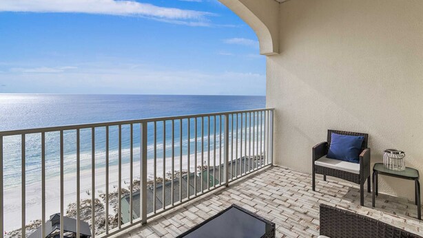 A balcony with a view of the ocean, a wicker chair with a cushion, and a small table with a candle holder. - Leeward Key 1203 2/2 Top Floor View for Miles, Beach Service, Renovated (Miramar Beach)