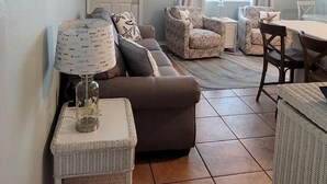 Una sala de estar con un sofá marrón, dos sillones estampados, una mesita y una lámpara.