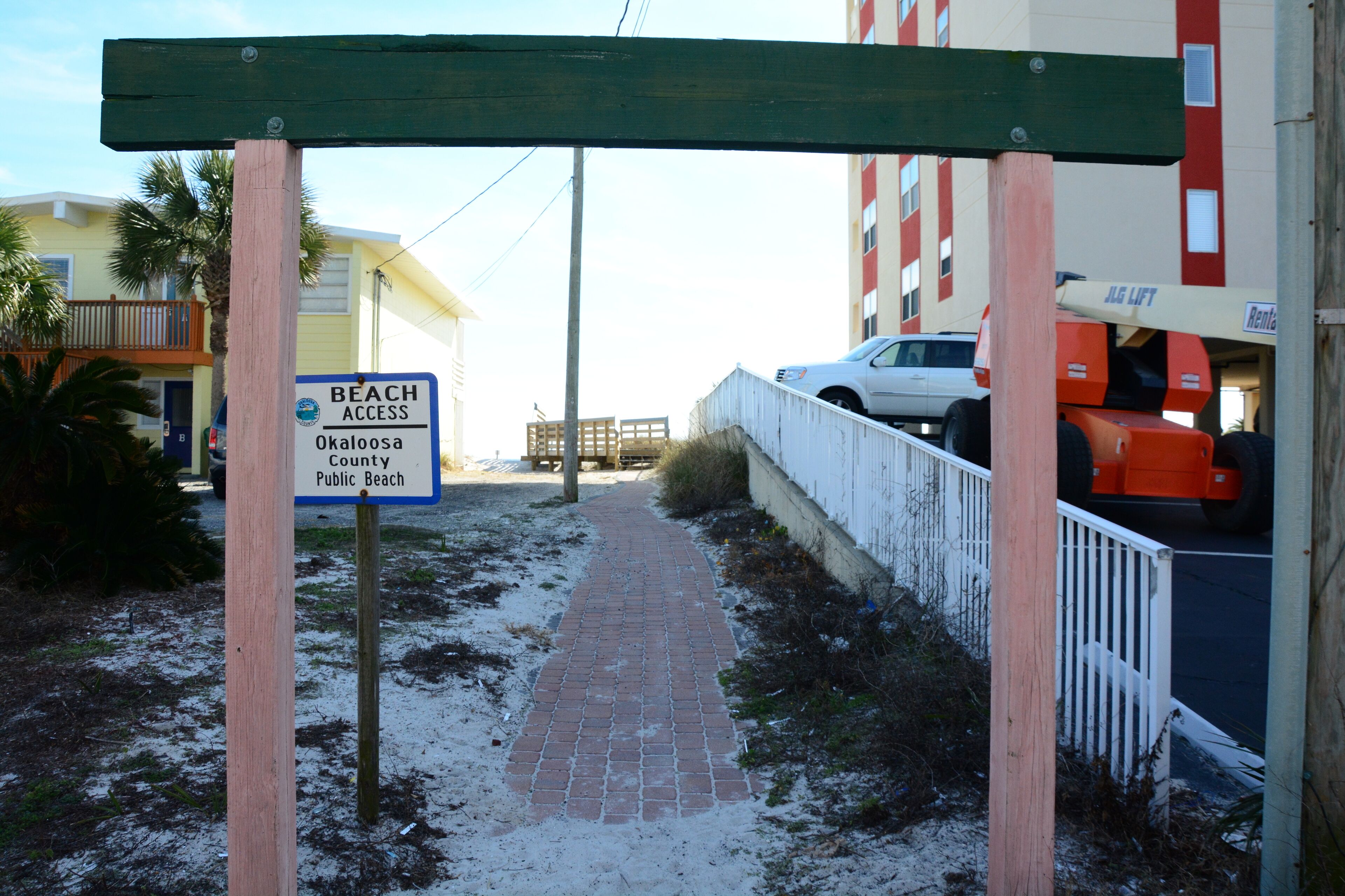 A pathway leading to a beach access sign for Okaloosa County Public Beach.
