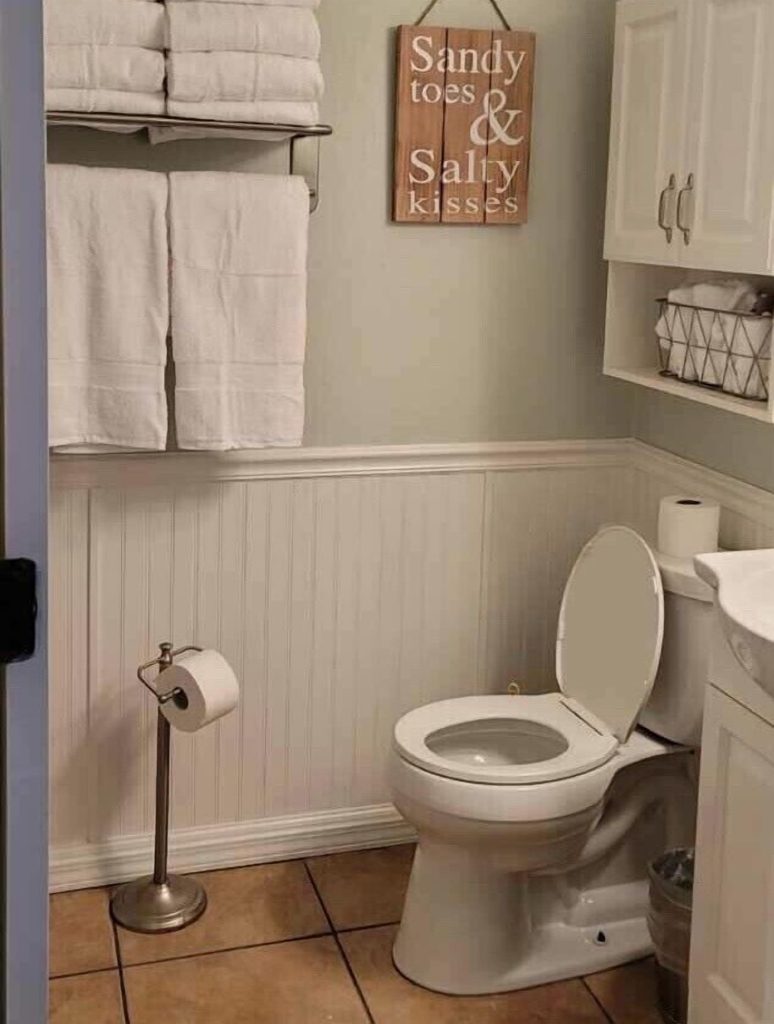 Ein Badezimmer mit Toilette, einer Toilettenrolle, einem Handtuchhalter mit gefalteten Handtüchern und einem Schild an der Wand.