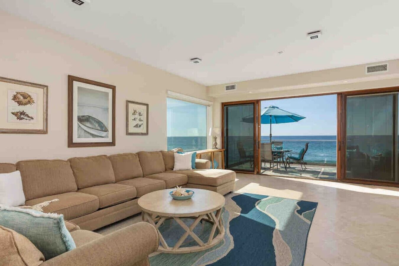 A spacious living room with a large sofa, a coffee table, and a view of the ocean through a sliding glass door.