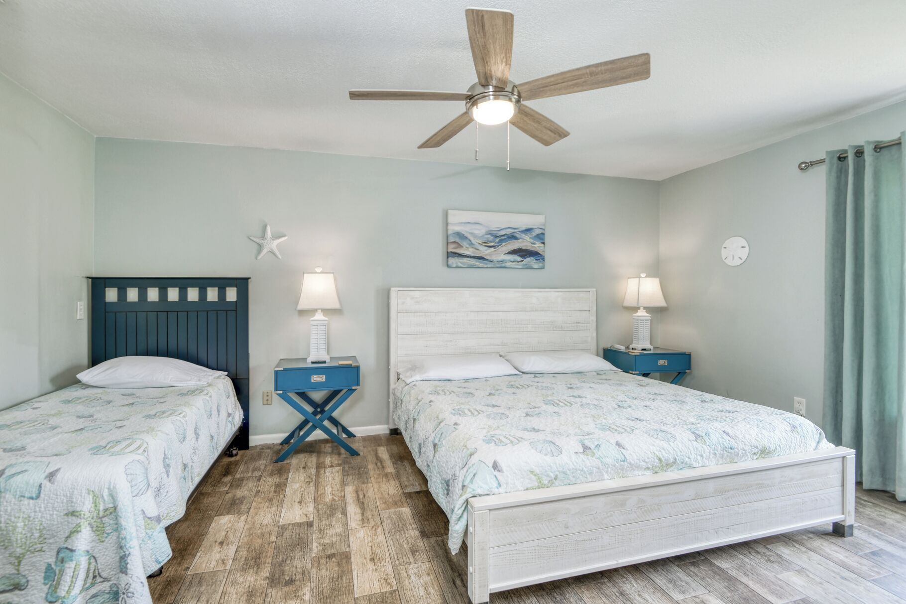 A bedroom with two beds, a ceiling fan, and a painting on the wall.
