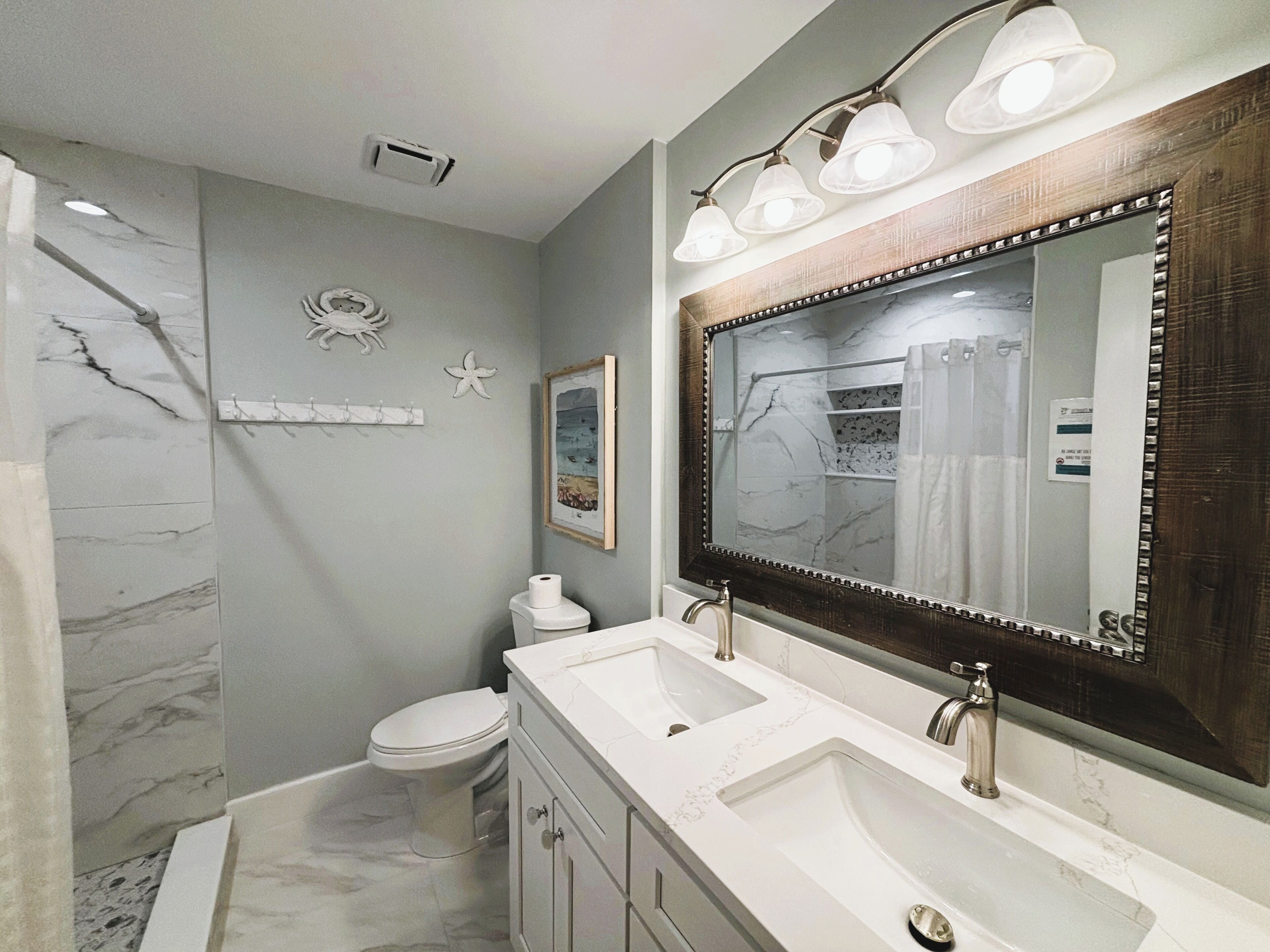 A bathroom with a large mirror, two sinks, a toilet, and a shower.