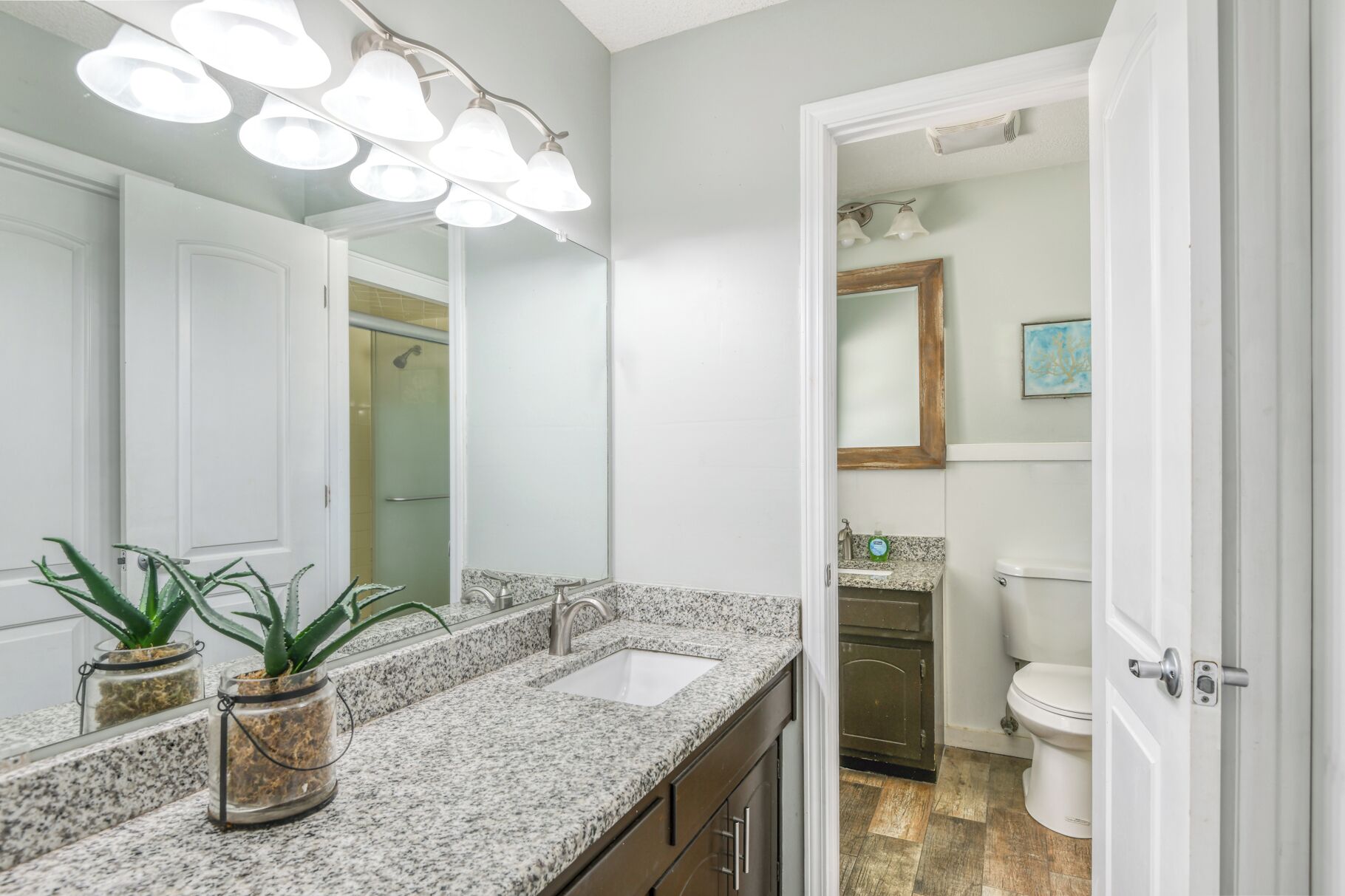 A bathroom with a granite countertop, a double sink, a large mirror, and a shower area.