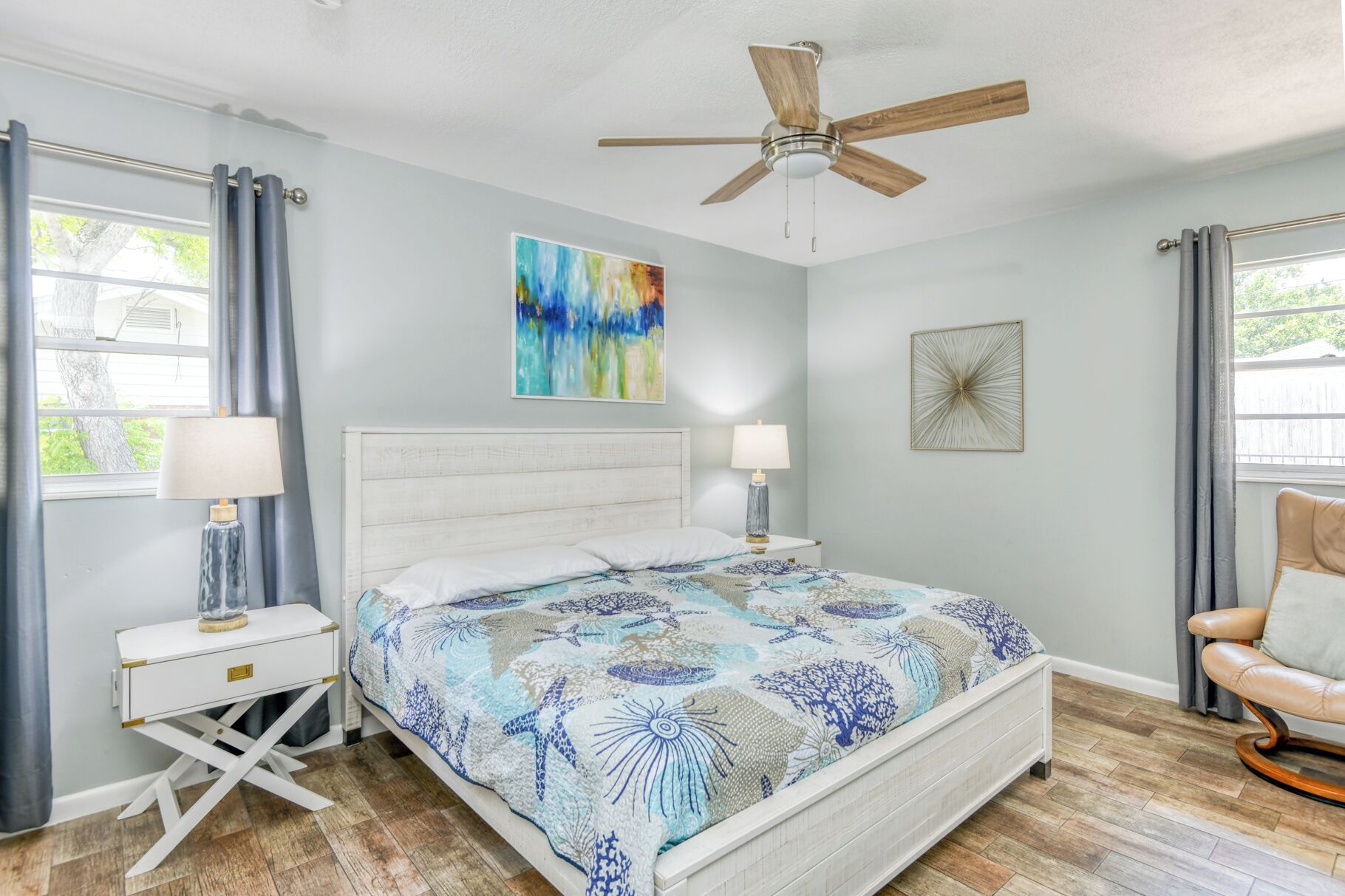 A bedroom with a bed, two bedside tables, a ceiling fan, and a window with curtains.
