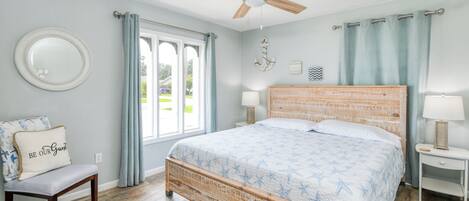 A bedroom with a wooden bed, a round mirror, a bench with a cushion, and a ceiling fan.