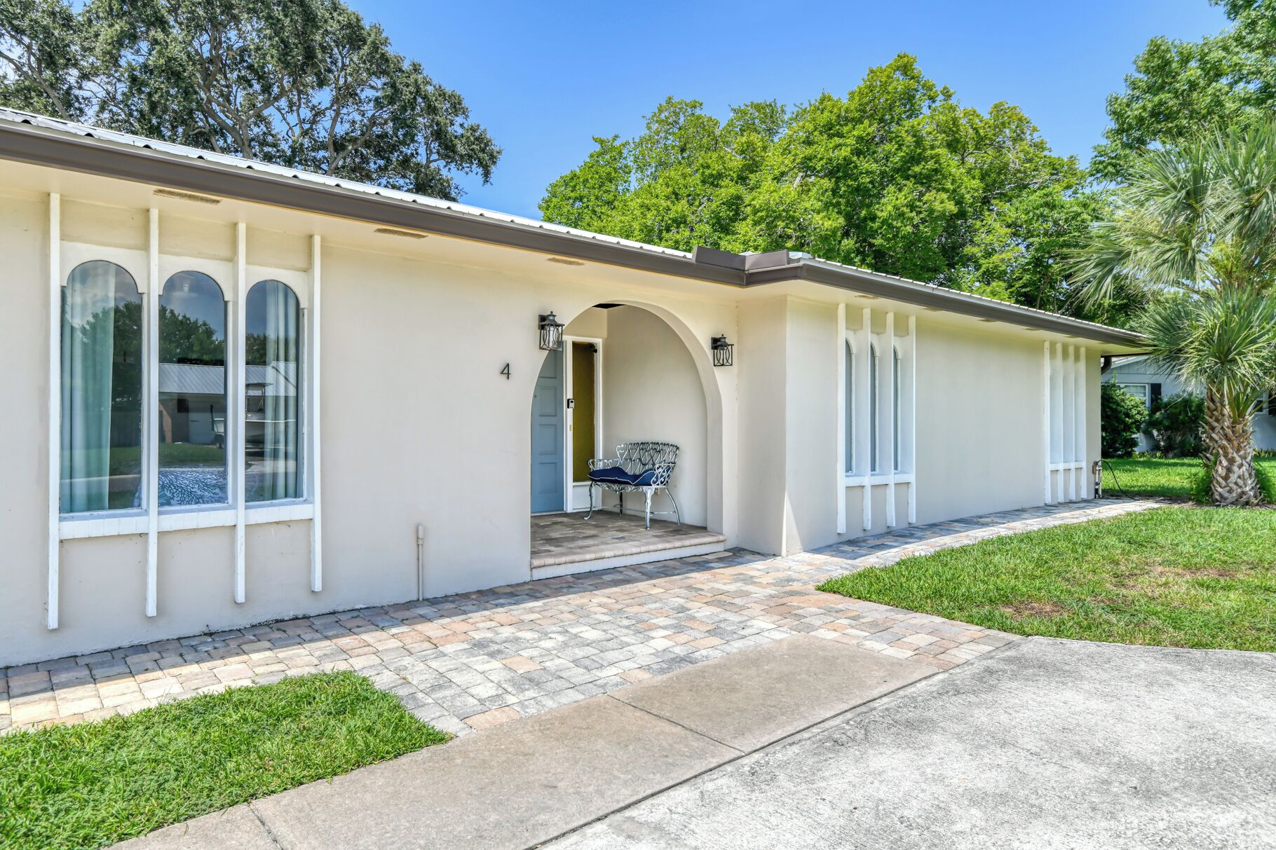 A single-story house with a covered porch, a small front yard, and a palm tree.