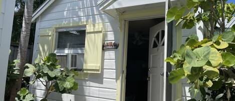 A small, single-story house with a white exterior, a front door, and a small porch area.