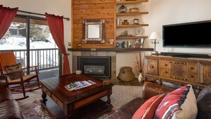 A cozy living room with a fireplace, wooden shelves, a television, and a comfortable seating area. - Spacious 3-Bedroom + Loft Condo at Timber Run – Mountain Views, and Walkable to (Steamboat Springs)