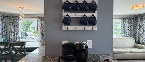 A kitchen with a coffee maker, a wall-mounted mug rack, and a dining area with a table and chairs.