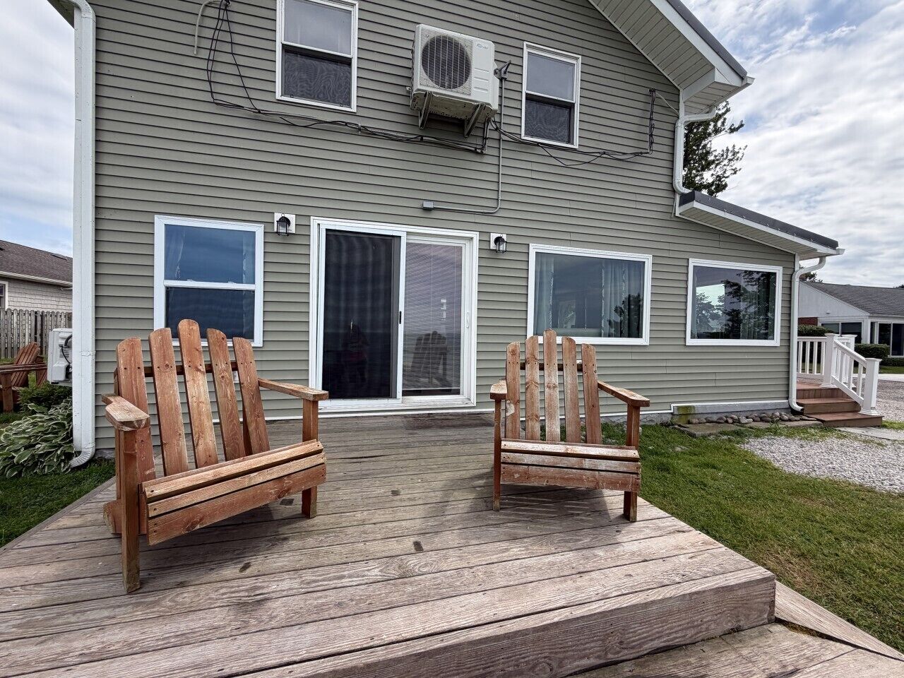 A two-story house with a deck, two Adirondack chairs, and a covered entryway.