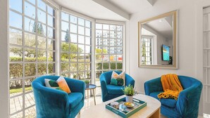 Una sala de estar moderna con ventanas amplias, dos sillones azules, una mesa de centro con objetos decorativos y un espejo en la pared.