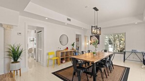 Un comedor amplio con una mesa de madera y sillas negras, una silla amarilla, una planta en maceta y una lámpara colgante moderna.