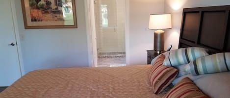 A hotel room with a bed, a nightstand with a lamp, a painting on the wall, and a door leading to a bathroom.