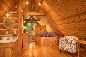 A wooden cabin interior with a bathroom, a bathtub, and a chair.