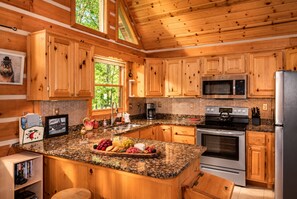 A kitchen with wooden cabinets, granite countertops, stainless steel appliances, and a fruit display.