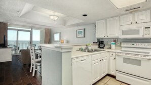 Une cuisine moderne avec des meubles blancs, un lave-vaisselle, une cuisinière et un four à micro-ondes. Il y a également un coin repas avec une chaise et une table.