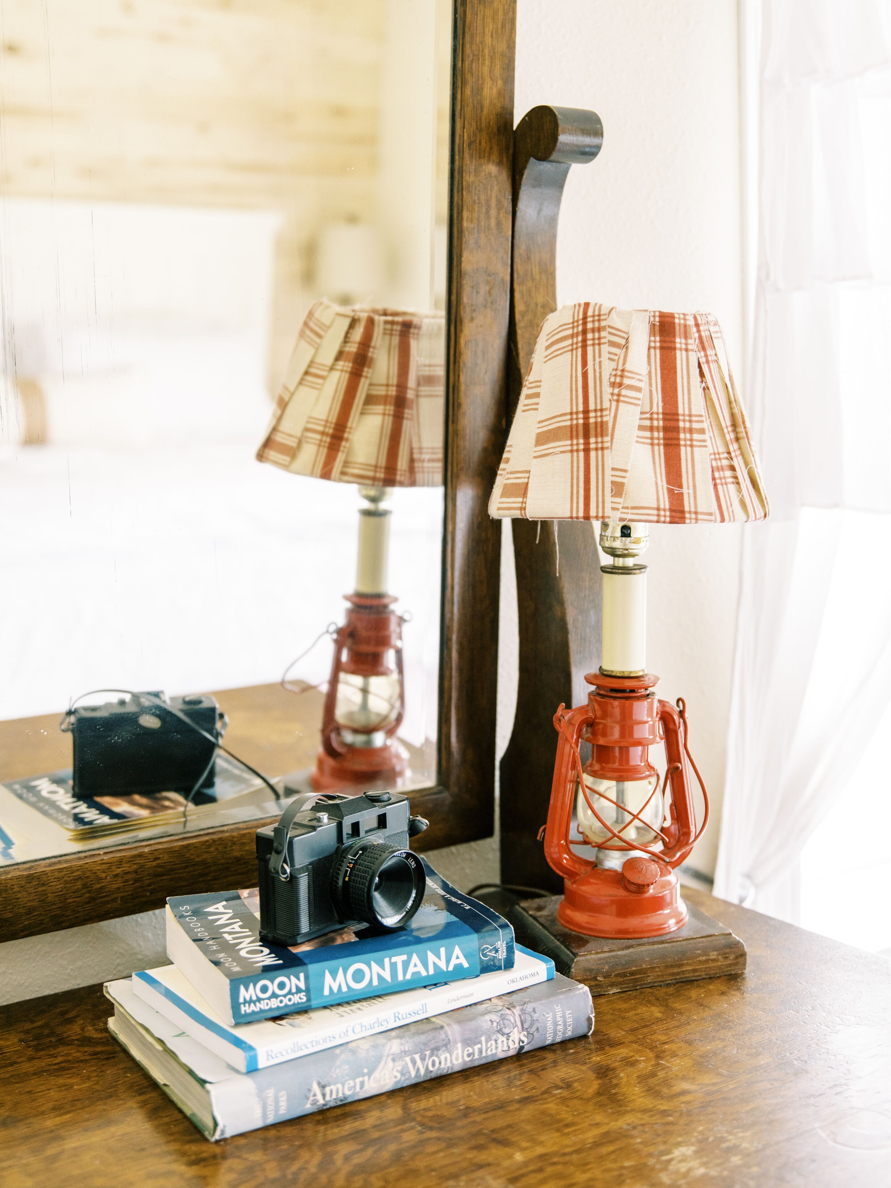 A wooden table with a camera, books, a plaid lamp, and a red lantern.