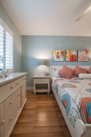 Een slaapkamer met een bed, nachtkastje, lamp en wanddecoratie.