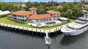 A waterfront property with a large house, a yacht docked at the pier, and a sign indicating 'IDLE SPEED NO WAKE'. - Waterfront Estate with Pool and Dock (Fort Lauderdale)