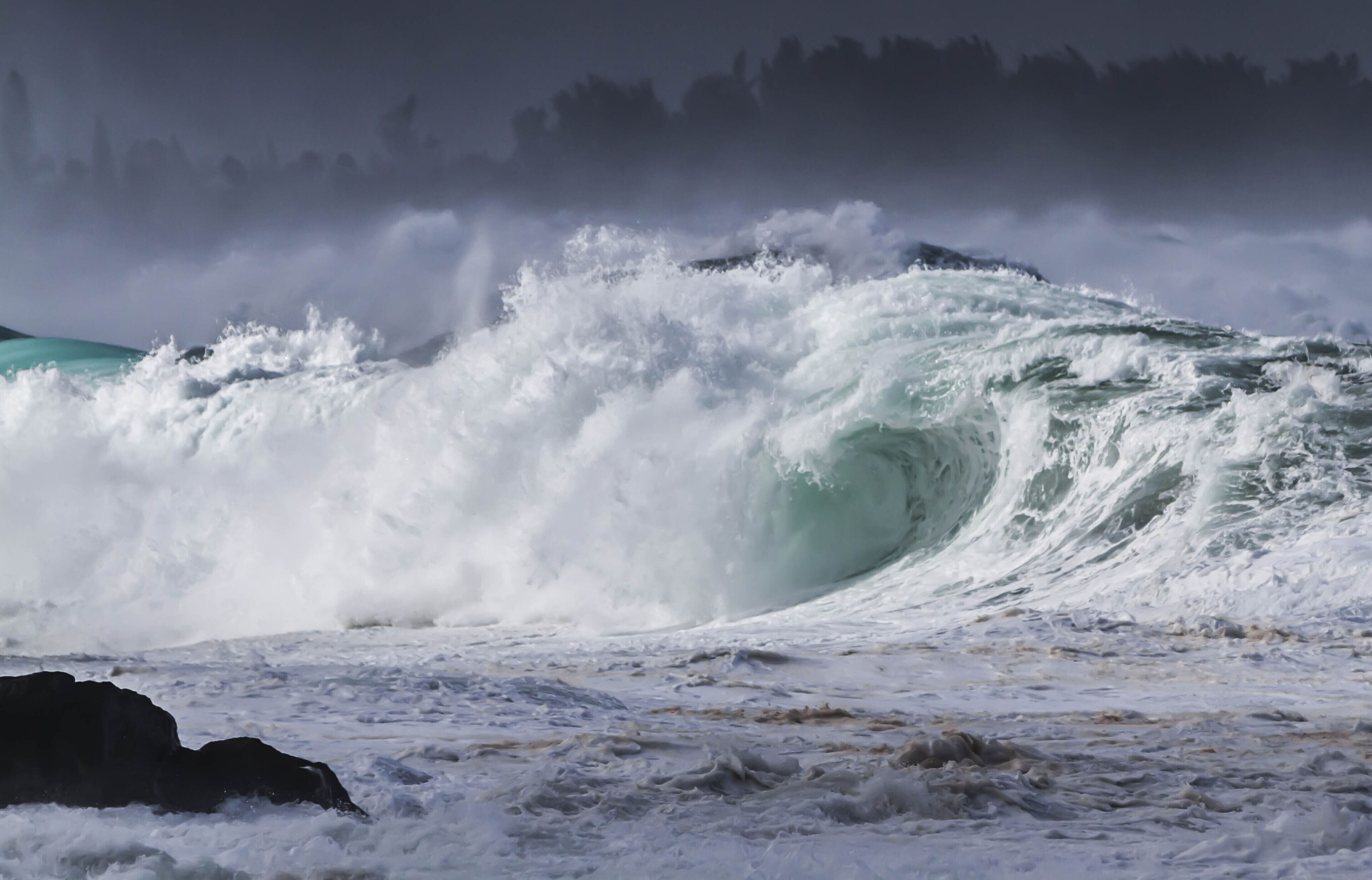 A large wave crashing onto a rocky shore.