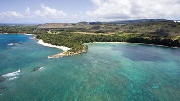 An aerial view of a coastal landscape with clear turquoise waters, a sandy beach, and a small island with dense vegetation.
