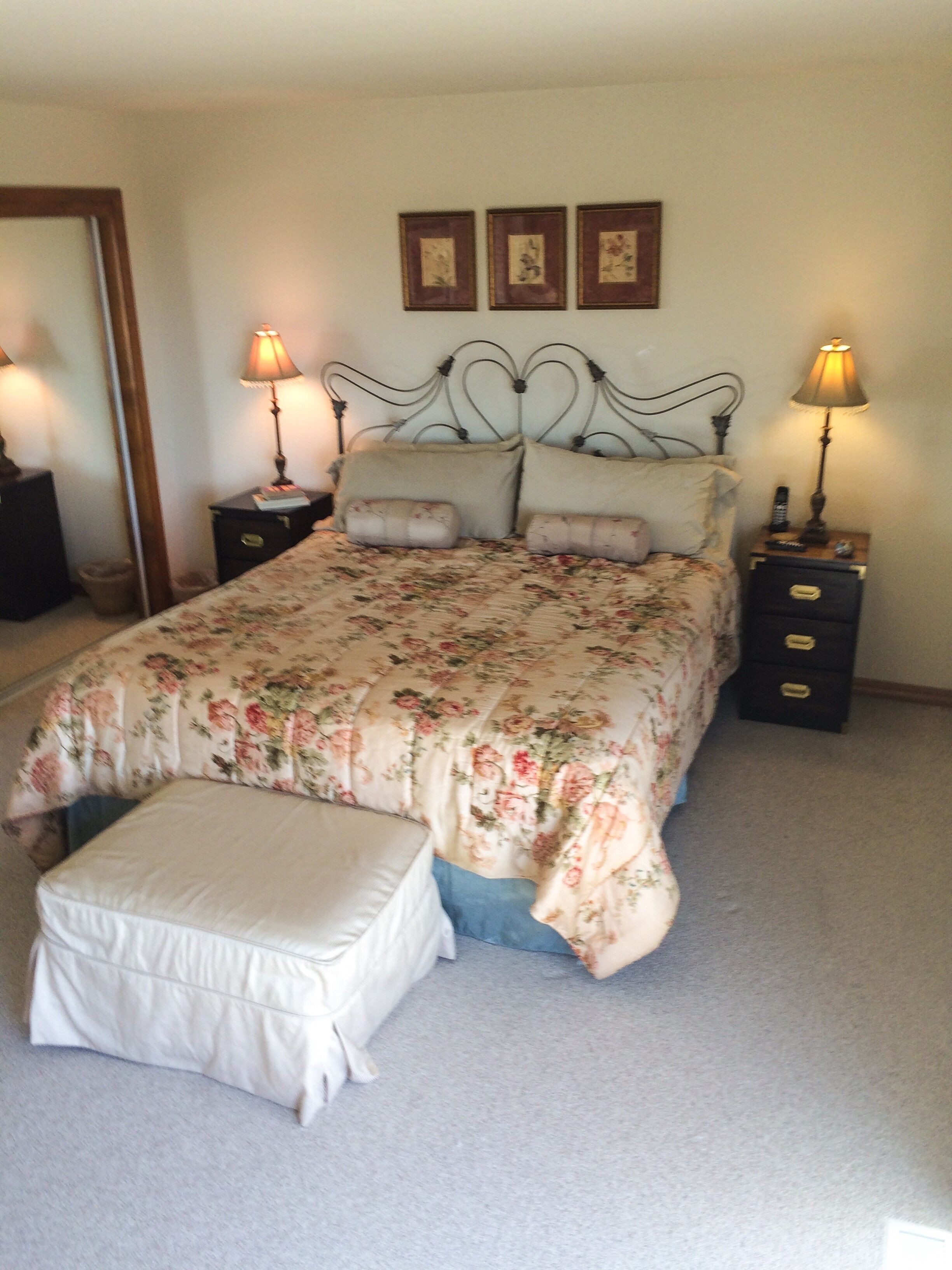 A bedroom with a bed, two bedside tables, a nightstand, a bench, and three framed pictures on the wall.