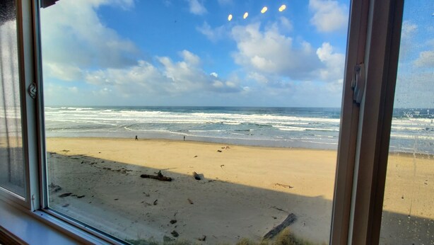 Vista a la playa desde una ventana, con arena y olas del océano.