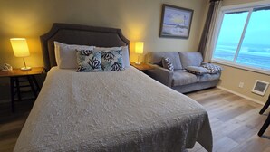 Un dormitorio con una cama grande, un sofá, dos lámparas de noche, un cuadro en la pared y una ventana con vistas.