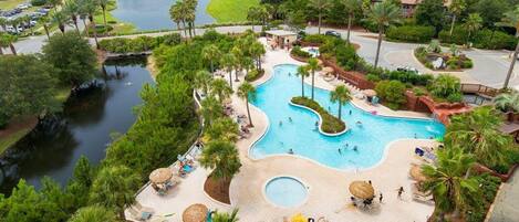 Un resort con una piscina central grande, una piscina circular más pequeña y un lago.