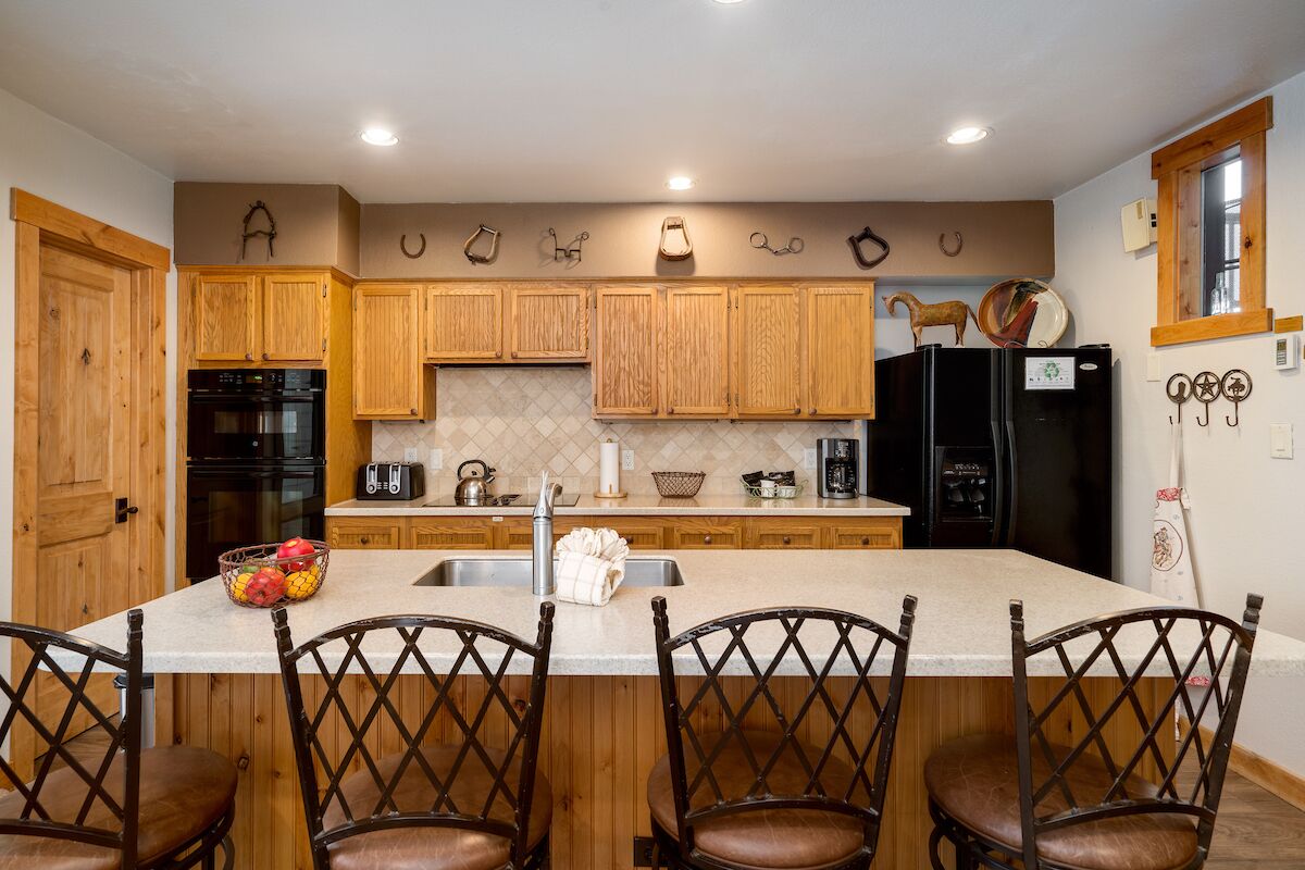 Una cocina con armarios de madera, una isla central con taburetes de bar, un refrigerador y un fregadero.